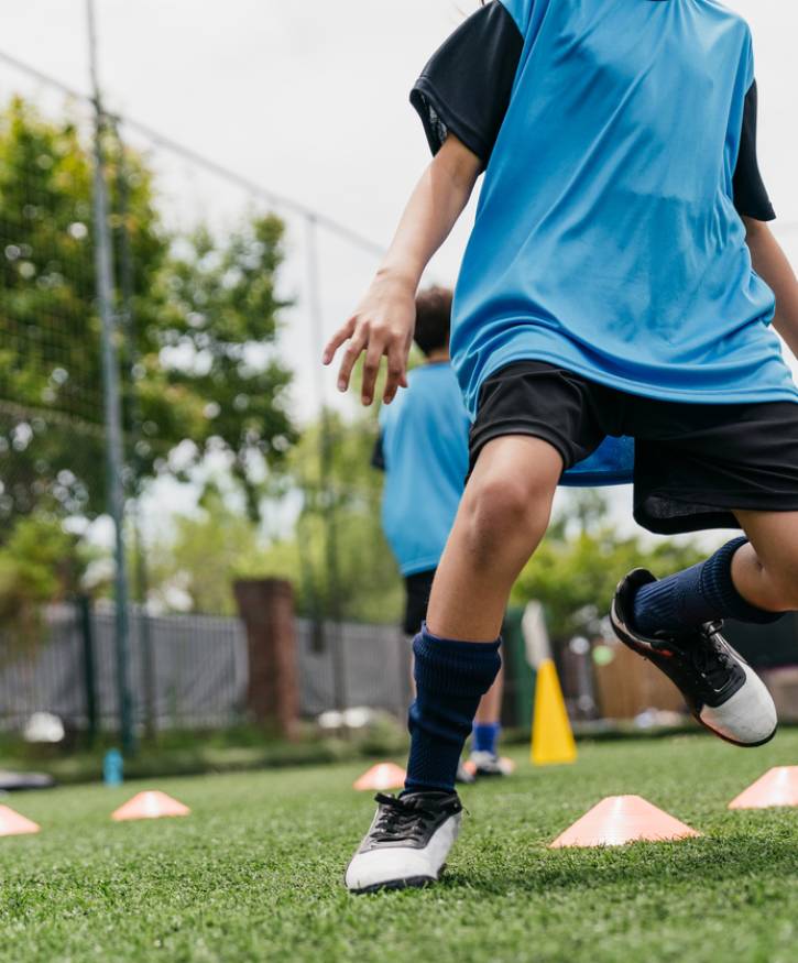 Low angle view of girls and boys practicing soccer drills. Determined football players are preparing for match with friends in background. They are in sports uniform.