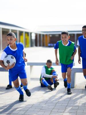 Schoolboys getting ready for soccer practice. Pulling on sock and shoes and greeting coach. School in rural area.
