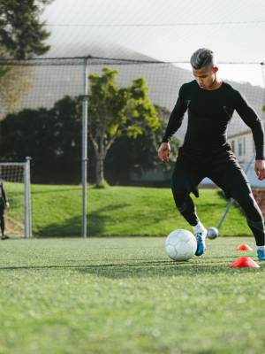 Young soccer player training in football field with team in background. Five a side football team practicing on field outdoors.